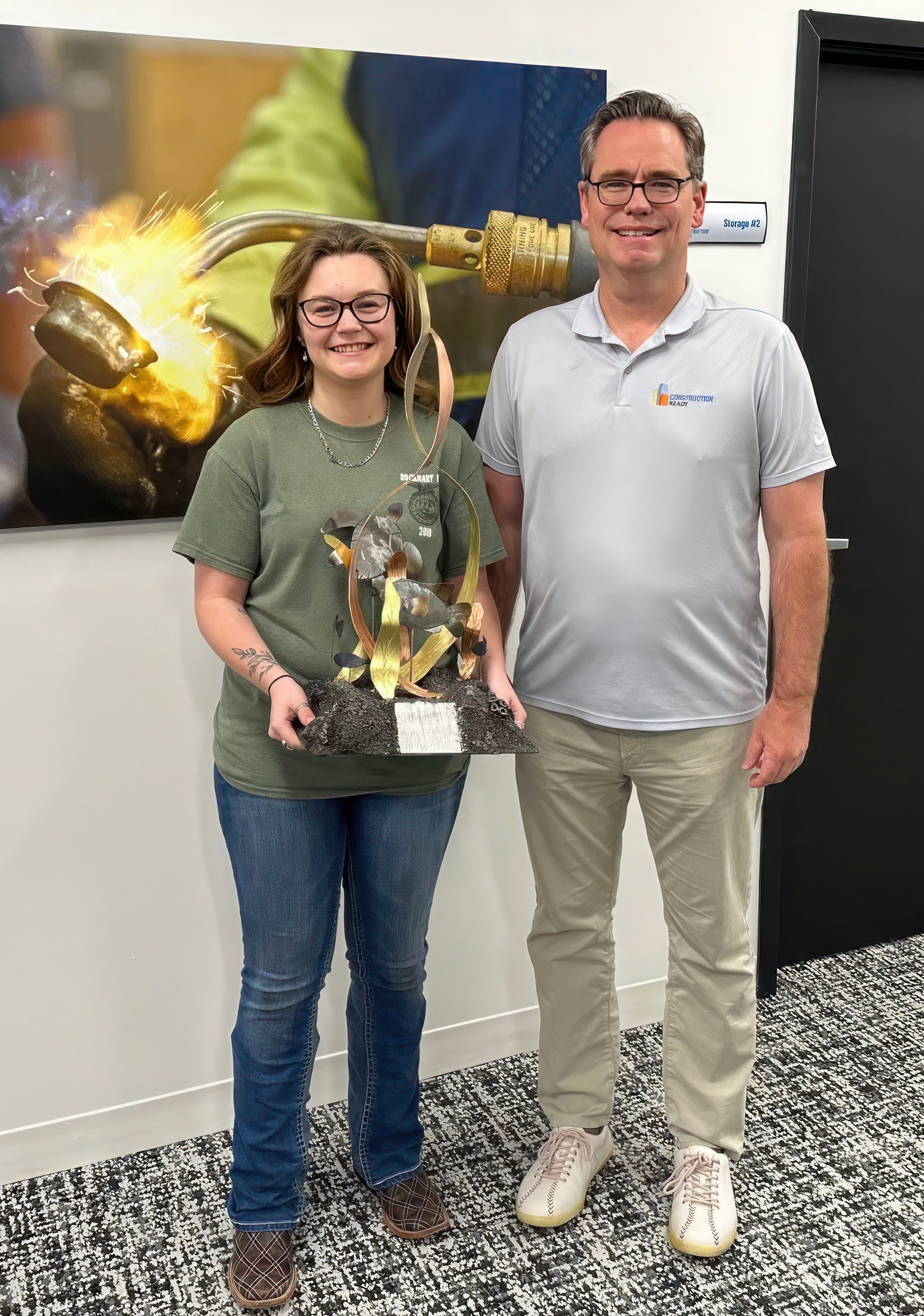 GNTC Welding and Joining Technology student Madison Gasho (left) presents Scott Shelar, president and CEO of Construction Ready, with the sculpture he commissioned as a gift for The Home Depot co-founder Bernie Marcus.